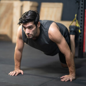 Handsome adult Caucasian men push up with trx robe to do crossfit exercise inside of fitness gym to workout for firm abs muscle and good body health.