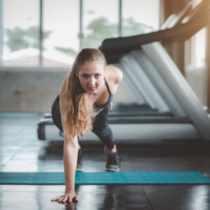 Beautiful caucasian woman doing one hand pushup exercisein in fitness gym
